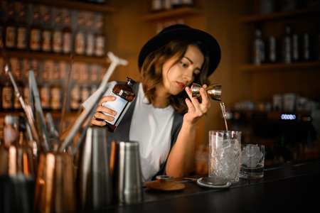 Female bartender pours clear drink from jigger into cocktail glassの写真素材