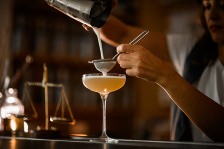 Female bartender straining frothy cocktail through a sieve into a tall stemmed glassの写真素材