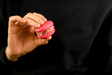 Chef in black uniform hold a macaron of a delicate pink color in her hands