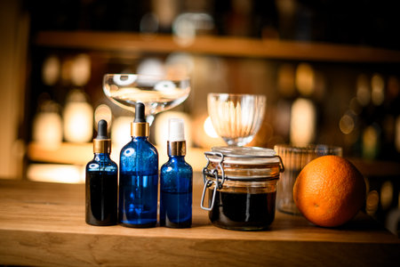 In the foreground are blue bottles with a dropper and a sprayer, a jar with jam and an orange