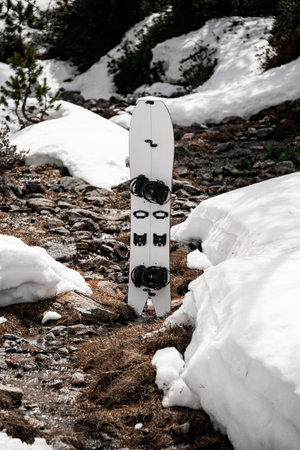 White splitboard stands on a stone where a thin mountain stream flowsの写真素材