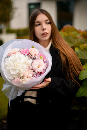 Pretty young woman neatly holding a delicate bouquet of various pink and white flowersの写真素材