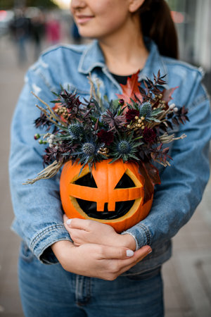 Flower arrangement of blue-headed flowers in a pumpkin with cut-out eyes and a mouth for the Halloweenの写真素材