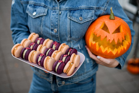 Woman shows off a plate with a set of colorful decorated macaroons in one hand, and a Halloween pumpkinの写真素材