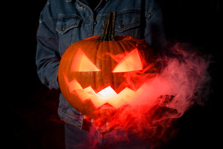 Scary Halloween pumpkin with a carved mouth and eyes in the dark in the hands of a young womanの写真素材