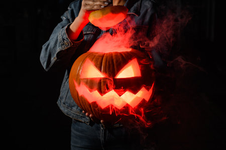 Scary Halloween pumpkin with a carved mouth and eyes in the dark and the lid removed in the hands of a young womanの写真素材