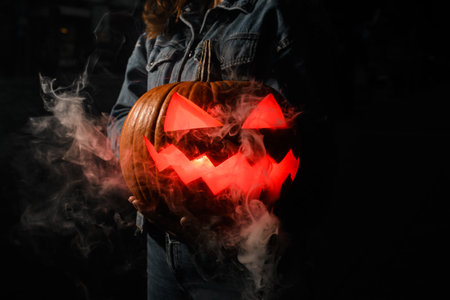 In the dark, a woman's hands hold a Halloween pumpkinの写真素材