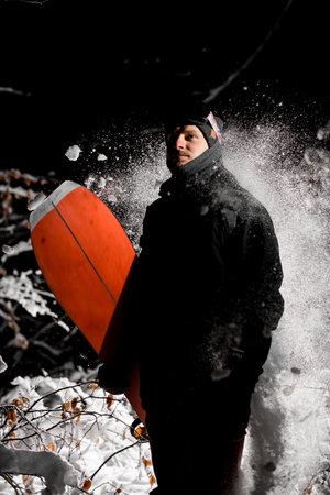 A young male snowboarder holds his splitboard in his hand