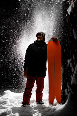 Young snowboarder in ski goggles looking to the side holds his splitboard with himの写真素材
