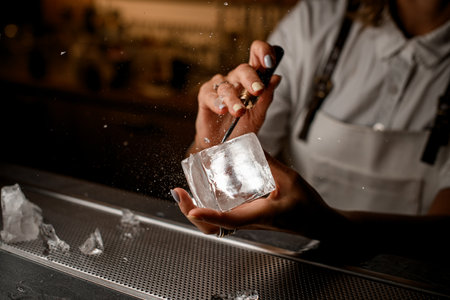 Female bartender hands holding an ice cube and chipping pieces of iceの写真素材