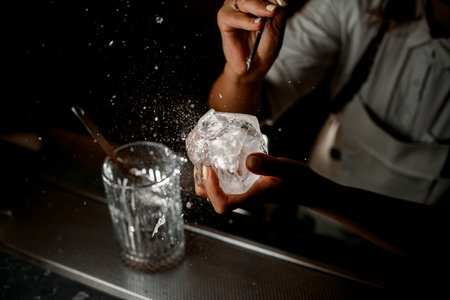 Female hands of a bartender holding an ice cube in one hand and chipping a small chip of ice intoの写真素材