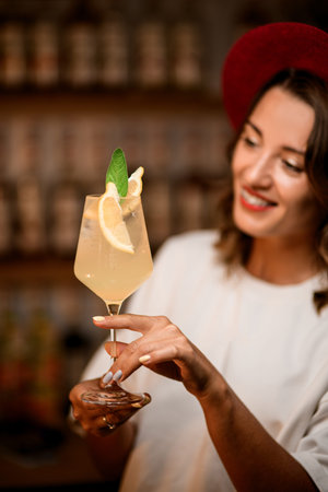 Focus on stemmed glass filled with white transparent cocktail with ice, lemon slices and green leaf