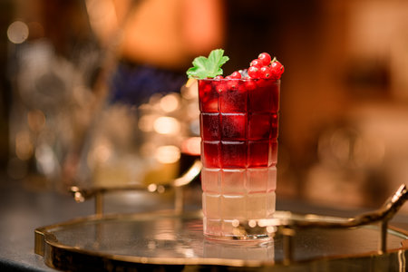 Close-up side view of a square-faced glass filled with a pink drink with red currantsの写真素材