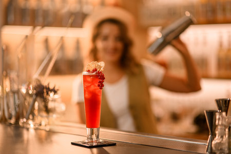 Tall thin glass filled with an orange drink and decorated with a bunch of red currants stands on the barの写真素材