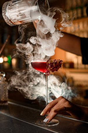Close-up of a glass on a very tall stem, filled with cocktail and decorated with a strip of foil