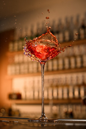 Glass on a tall stem stands on the bar counter, from which splashes of drink fly in different directionsの写真素材