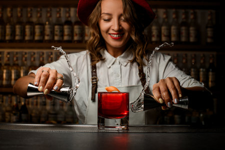 Happy female bartender holds a jigger with a transparent drink in both hands, which she pours on each otherの写真素材