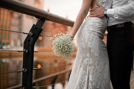Close-up photo of a brides bouquet in her hands, with her groom hugging her waist near the railing...