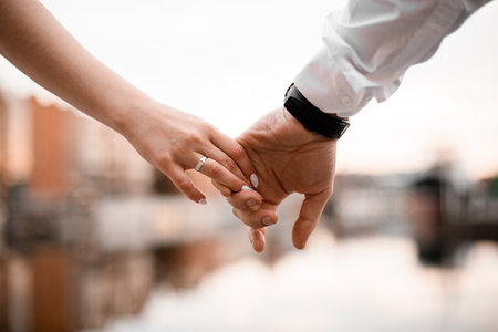 Close-up of the grooms hand holding the brides hand by the fingers, on one of whose fingers is wearing a wedding bandの写真素材