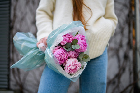 Focus on a beautiful bouquet of pink peonies in the hands of a young womanの写真素材
