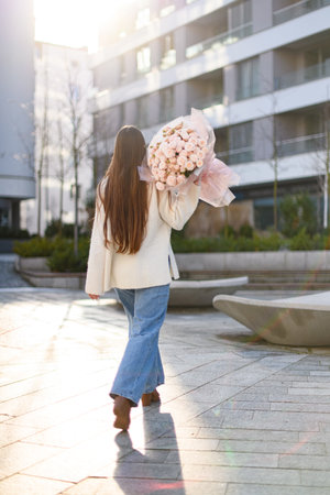 Turn away girl with straight hair going on a street with a bouquet of rosesの写真素材