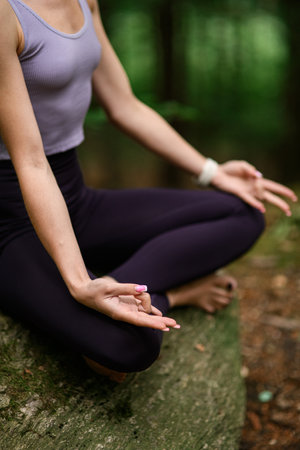 Young woman practicing yoga outdoors, sitting on large stone in natureの写真素材