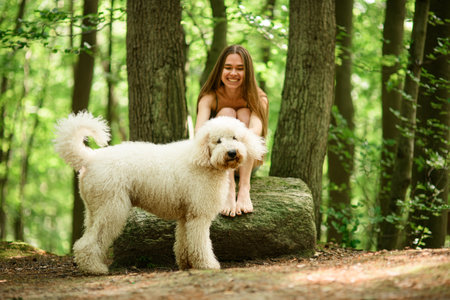 Cute happy woman sitting on a stone and smiling sincerely looking at the dog standing next to herの写真素材