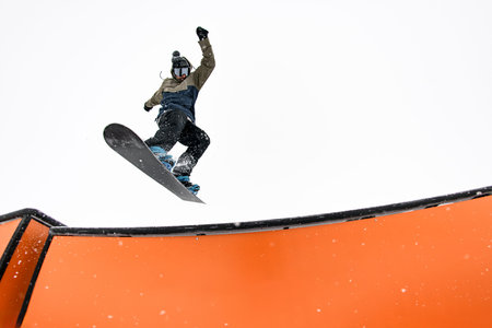 Jumping pro snowboarder engages wallride, displaying expertise on slopes.