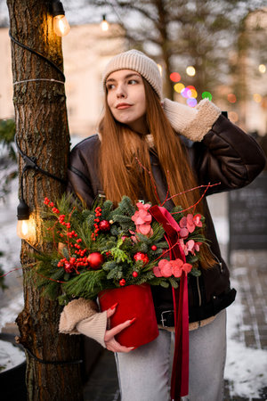 Young woman, looking to the side, holding a Christmas bouquet, decorated in red styleの写真素材
