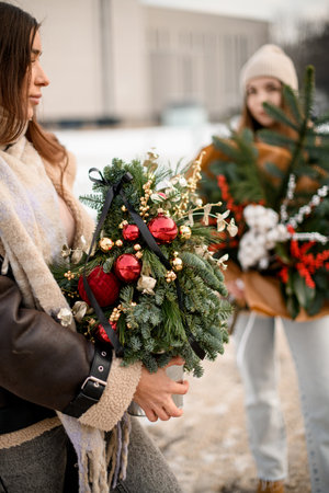 In the foreground, a woman holds a bouquet of Christmas tree branches in the shape of a small Christmas tree with toysの写真素材