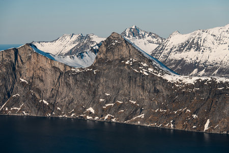 The blue sea at the foot of the rocky cliff of the mountain, behind which many sharp peaks can be seenの写真素材