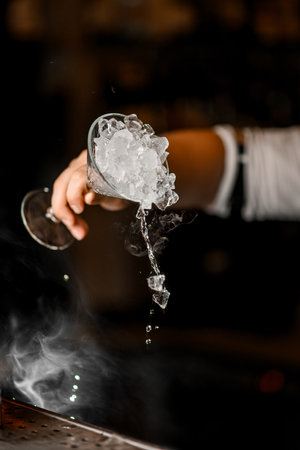 Male bartenders hand slowly flips a martini glass filled with iceの写真素材