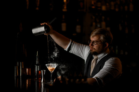 Side view of the process of making a cocktail as the bartender pours the finished drink into a glassの写真素材
