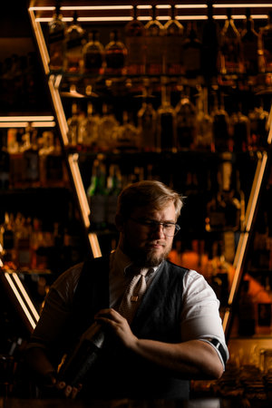 Male bartender with shaker holding with two hands, looking to the side and standing behind the barの写真素材