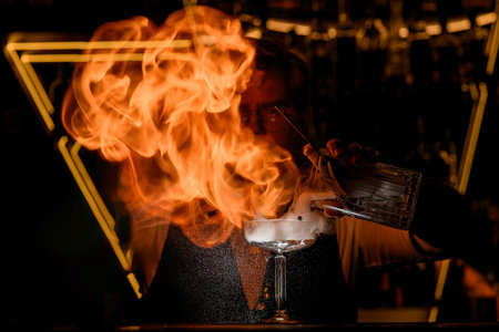 Bartender pours a cocktail from a mixing glass into a glass while directing a flame at itの写真素材