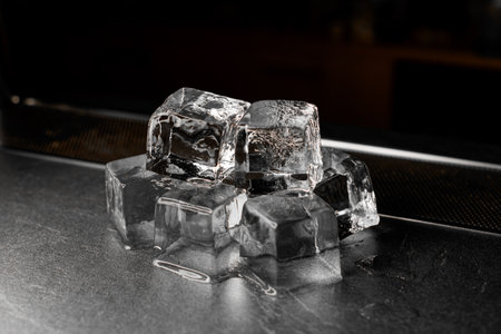 Several large ice cubes lie on the bar counter, glistening with their crystalline facesの写真素材