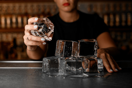 There are huge ice cubes on the bar counter that are slowly melting, one of which is held by a female bartenderの写真素材