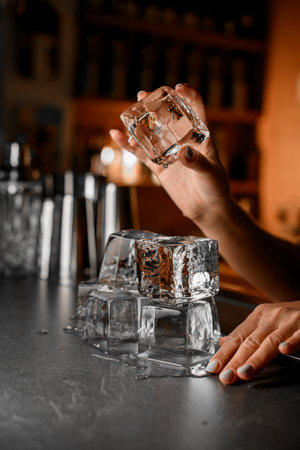Side view of a womans hand carefully holding an ice cube over other ice cubesの写真素材