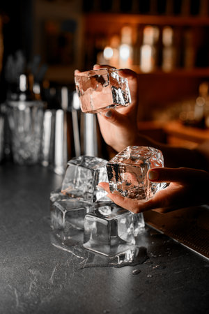 Side view of female hands carefully holding one ice cube on top of other ice cubes on bar counterの写真素材