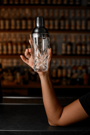 Female hands of bartender holding glass shaker with steel lidの写真素材
