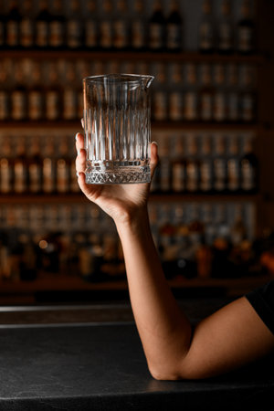 Female hands of a bartender holding a glass cocktail mixing glass with a spout for easy pouringの写真素材