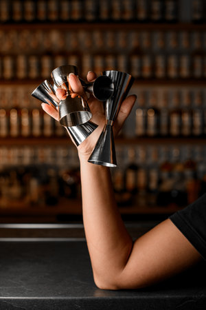 Female hands of a bartender holding between her fingers four steel jiggers of different sizes and shapesの写真素材