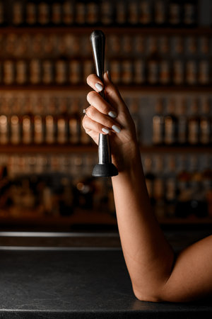 Female hands holding a stainless steel muddler with a black tip