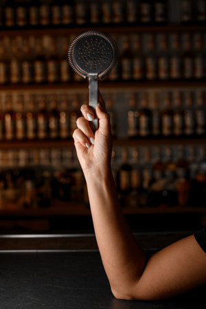 Female hands of bartender holding hawthorn steiner for straining cocktails while pouring into glassの写真素材