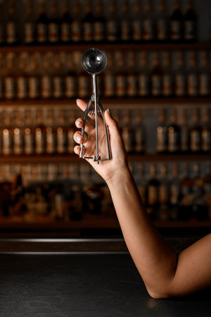 Female hands holding a spoon for forming large scoops of ice cream with special springs on the handleの写真素材