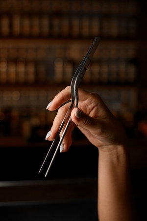 Female bartender hands holding bent barmans tweezers for holding various solid cocktail ingredientsの写真素材