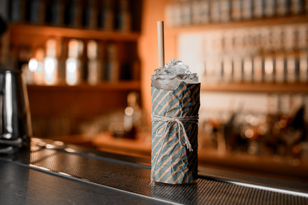 On the bar stands a tall glass, wrapped in gift paper and tied with a white thread from a cocktailの写真素材