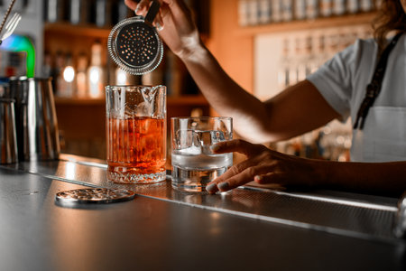 Female bartender hand holds a cocktail strainer over a mixing glassの写真素材