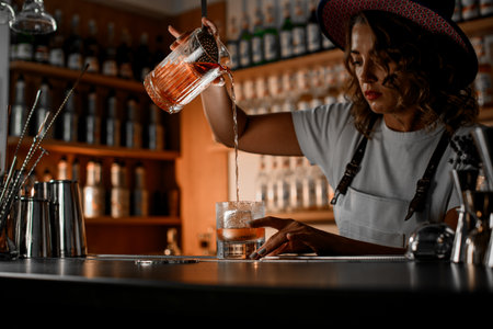 Female bartender preparing a cocktail while standing behind the bar on a blurred backgroundの写真素材