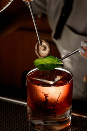 Glass with a brown cocktail and an ice cube stands on a bar counterの写真素材